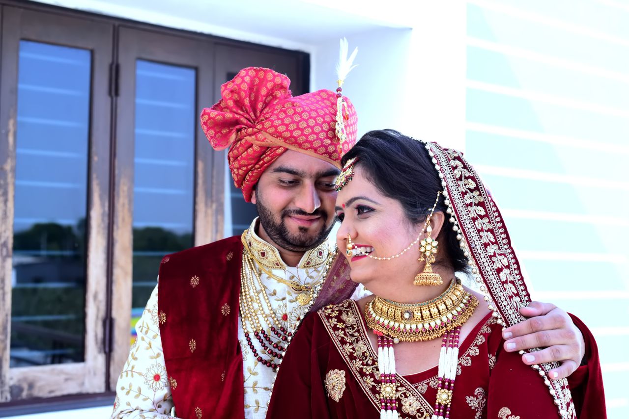 South Asian couple in traditional wedding attire sharing a joyful moment indoors.