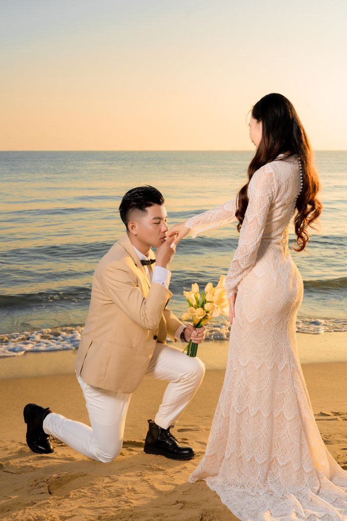 A romantic beach proposal with the groom kneeling for his bride by the seashore during sunset.