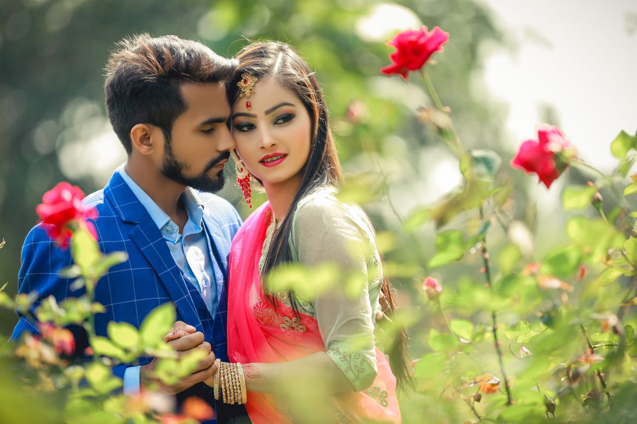 Elegant couple in formal attire embracing among blooming roses in Amsterdam, Netherlands.