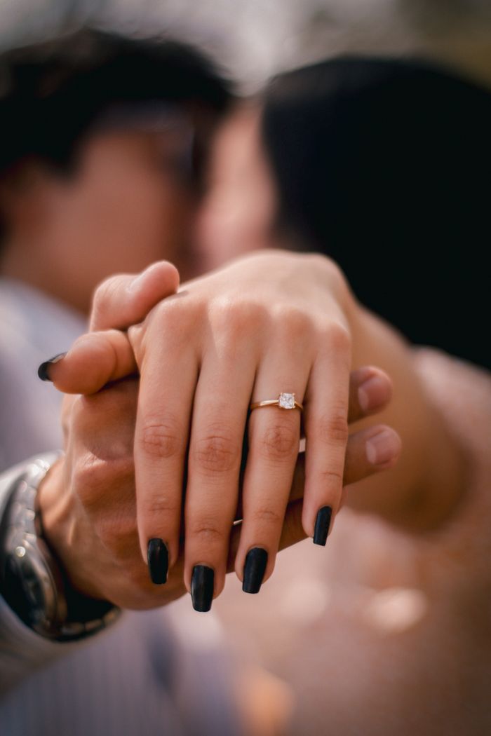 Close-up of a couple holding hands, showcasing an engagement ring.