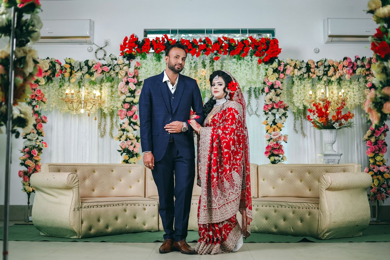 A bride and groom pose indoors with vibrant floral decorations at their wedding ceremony.