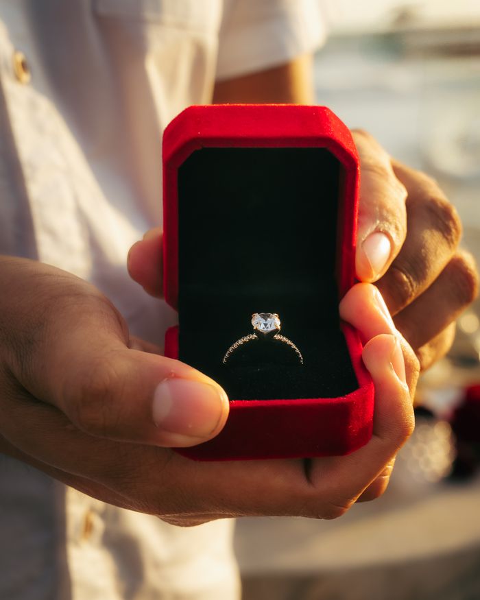 Close-up of a diamond engagement ring in a red velvet box held by a person, symbolizing love.