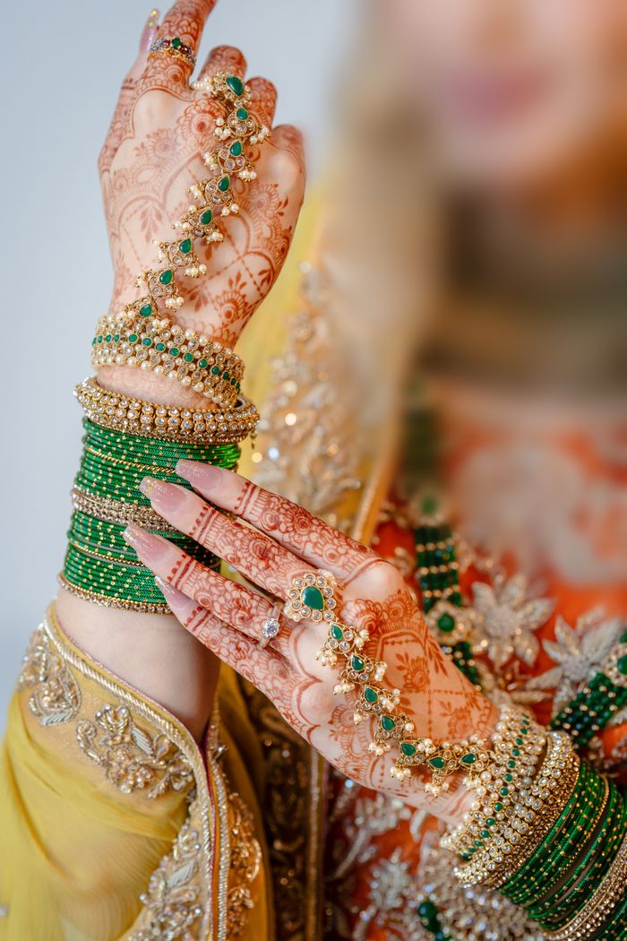 Close-up of intricate henna designs and jewelry on a bride's hands with green bangles.