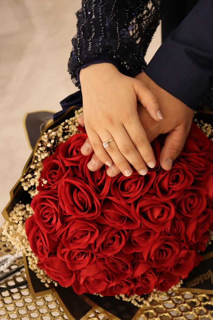 Close-up of hands with engagement ring over a bouquet of red roses, symbolizing love.